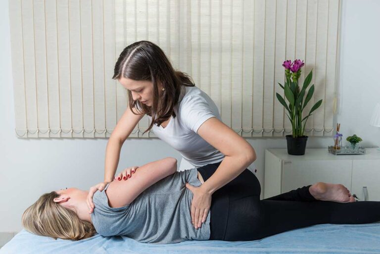 A person squatting with straight posture to lift a cardboard box from a living room floor.